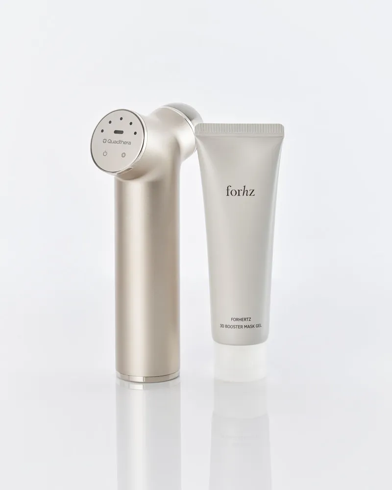 Quadthera Titan ultrasonic facial device in champagne finish beside a tube of FORHERTZ gel, on a light background